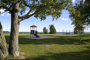 Un parque con un área de juegos, un árbol grande y vistas al agua.