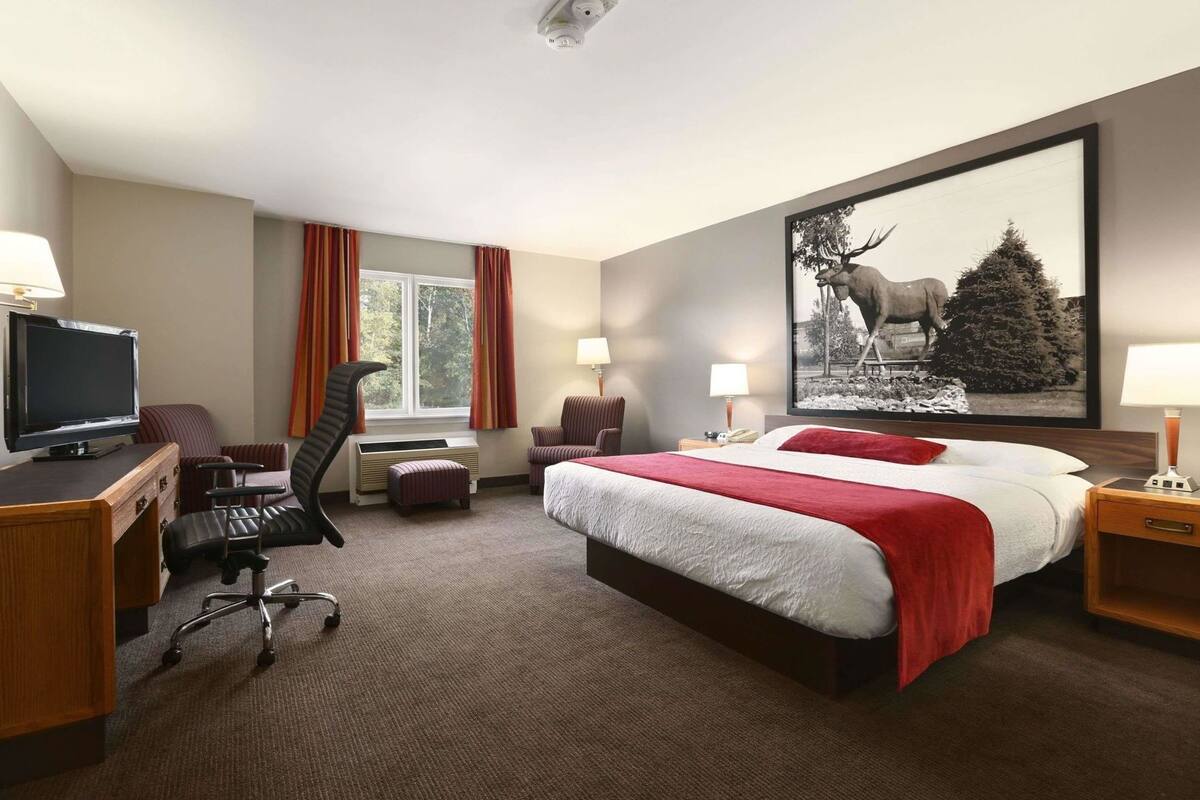 A hotel room with a bed, desk, chair, TV, and a large wall painting.