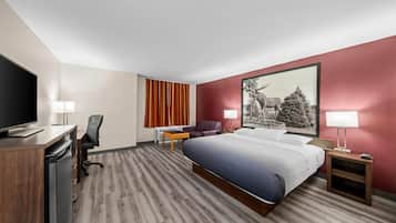 Ein Hotelzimmer mit Bett, Schreibtisch, Stuhl, Fernseher und einem Bild an der Wand.