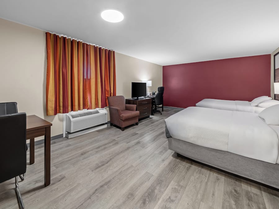 A hotel room with a bed, a desk with a computer, a chair, a heater, and a TV.