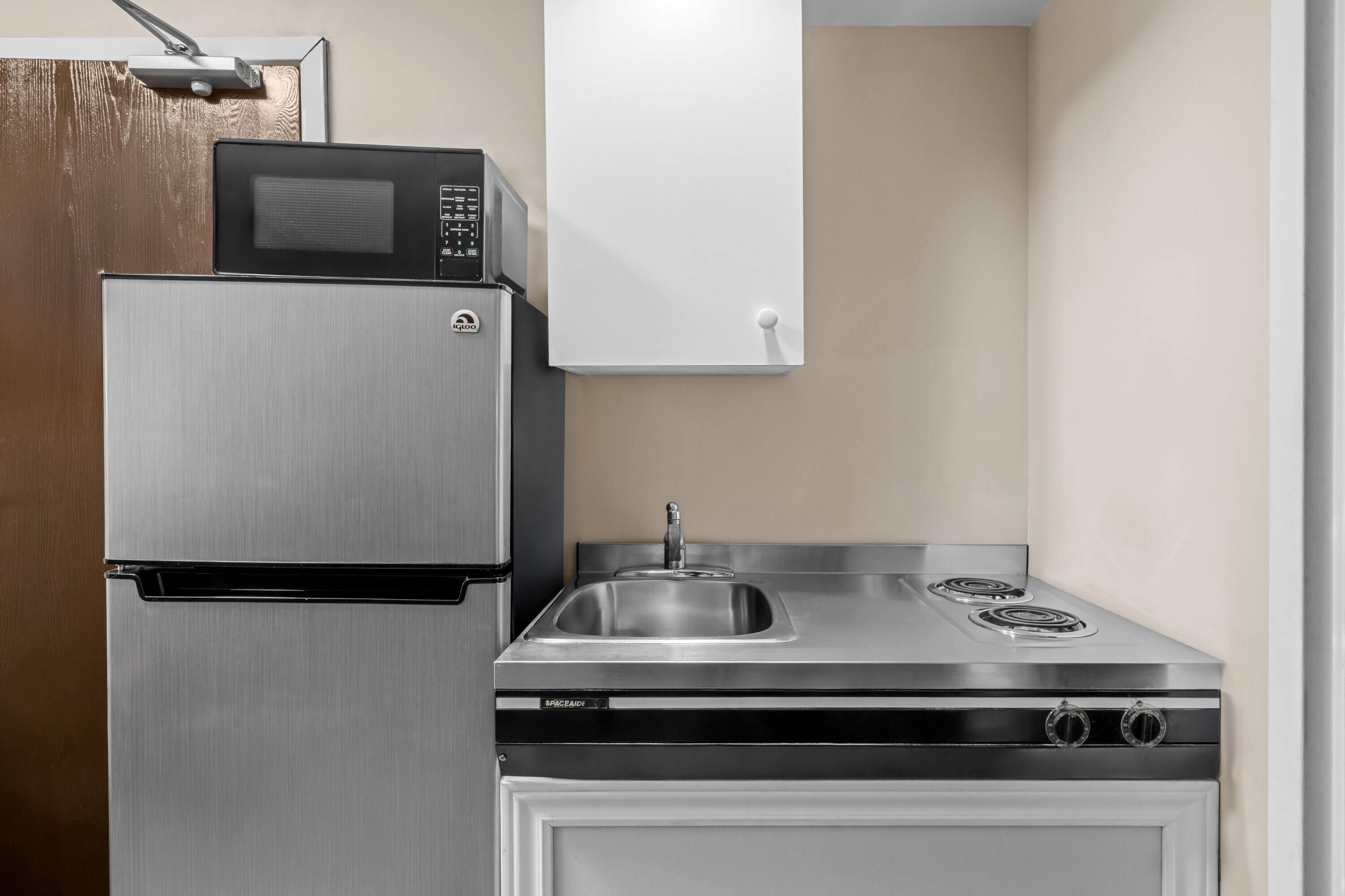 A compact kitchen with a stainless steel refrigerator, a microwave, and a stove with a sink.
