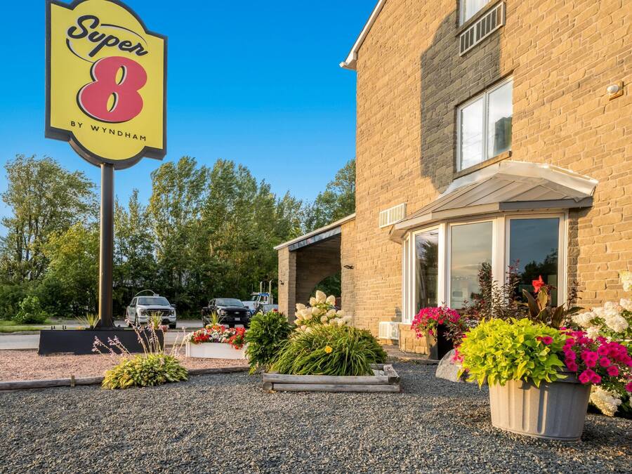 A hotel entrance with a prominent sign, a brick building, and a parking area.