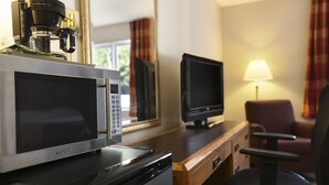 Una kitchenette con microondas, cafetera y televisor sobre un escritorio de madera.