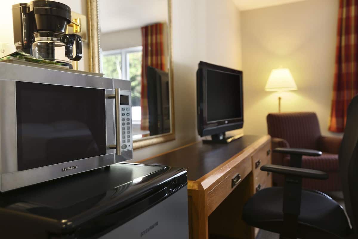 A kitchenette with a microwave, coffee maker, and a television on a wooden desk.