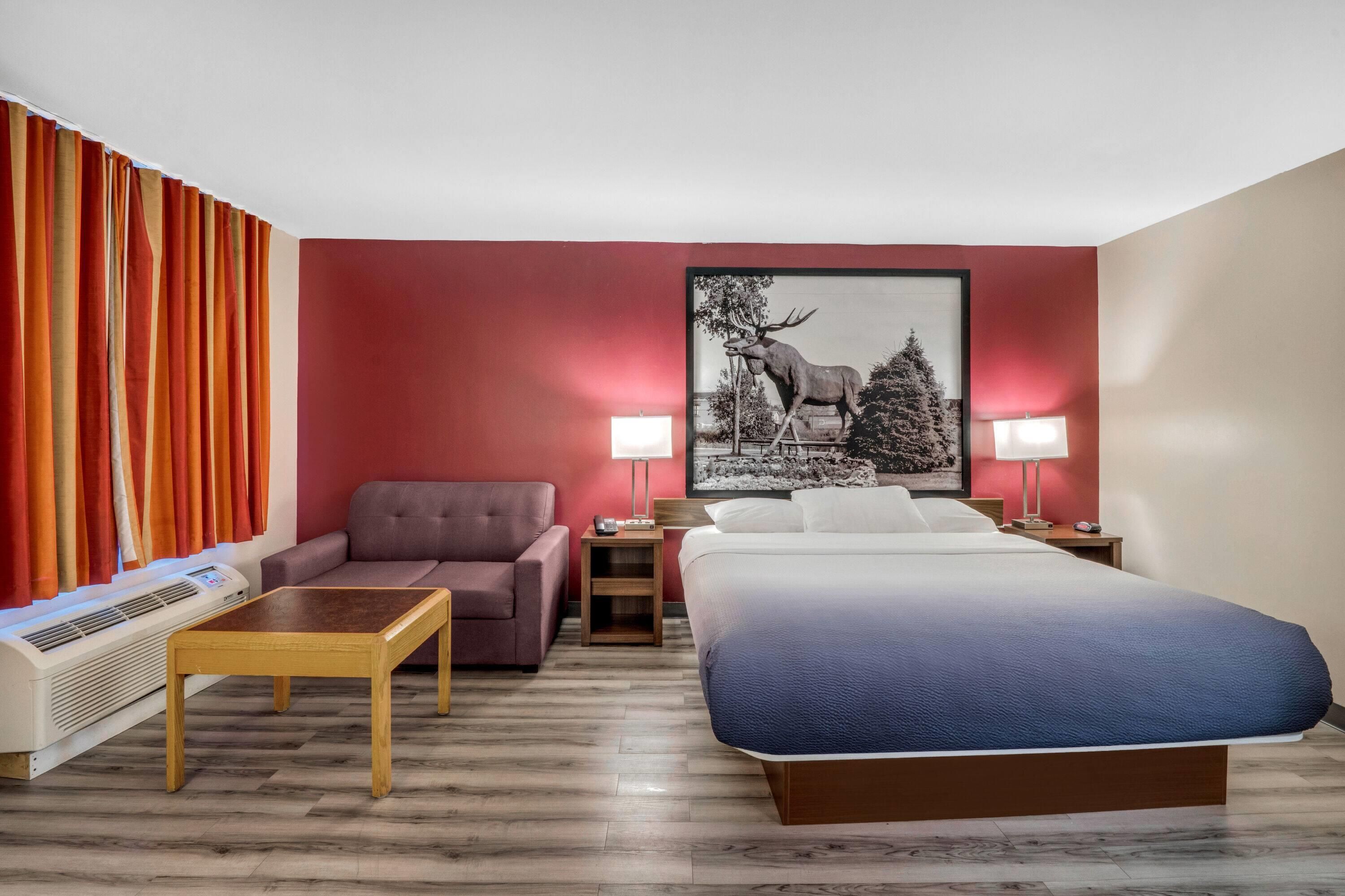 Een hotelkamer met een bed, een bank, een eettafeltje, een lamp en een schilderij aan de muur.