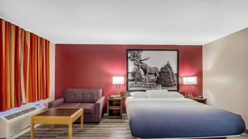 A hotel room with a bed, a sofa, a small table, a lamp, and a picture on the wall.