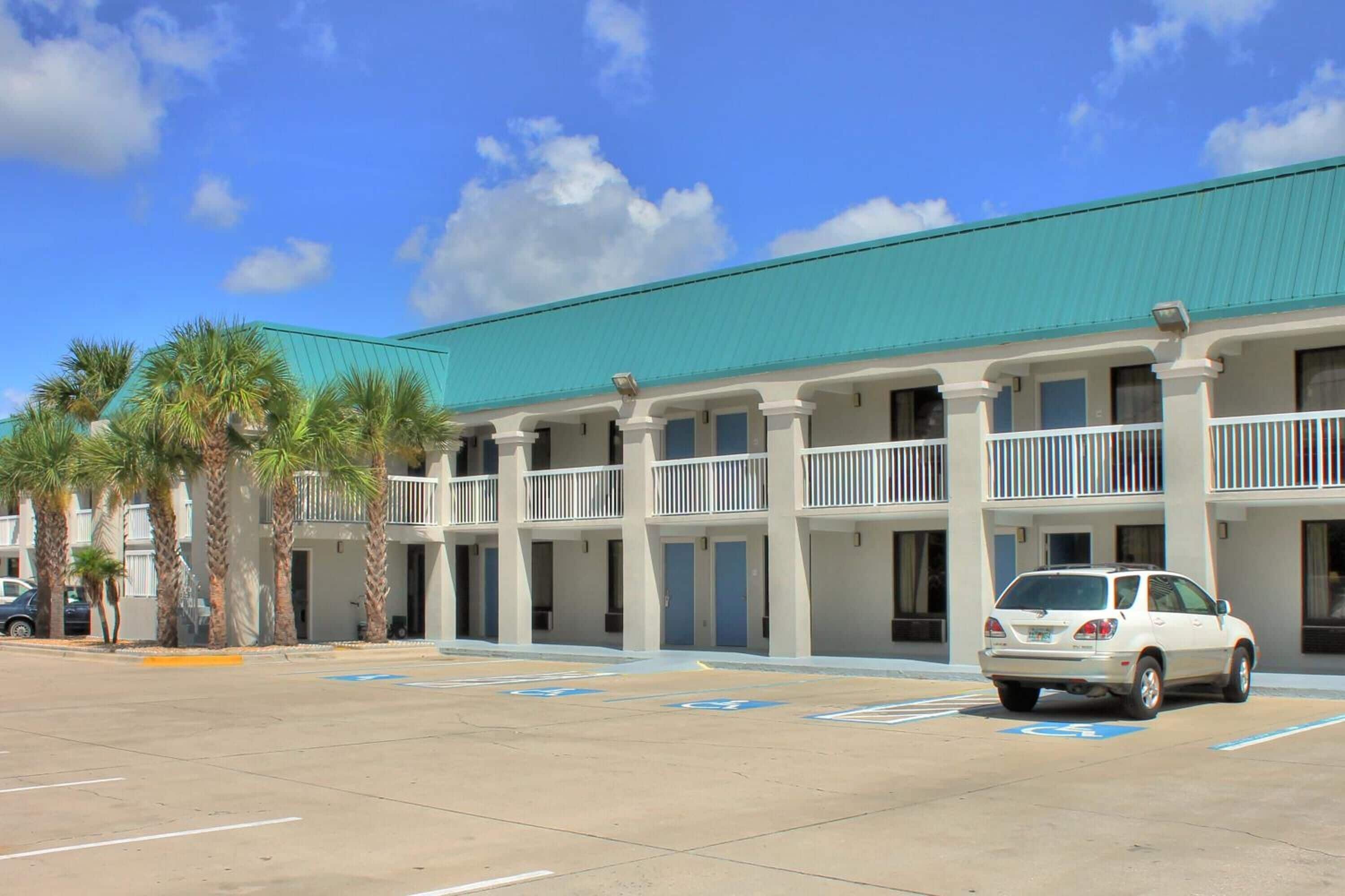 A hotel with a green roof, multiple balconies, and a parking lot with handicapped spaces.