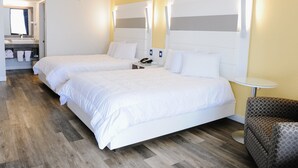 A hotel room with two beds, a small round table, a sofa, and a bathroom visible through an open door.