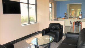 A modern living room with a glass coffee table, black leather sofas, and a flat-screen TV mounted on the wall.