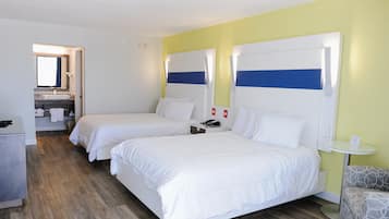 Une chambre d’hôtel avec deux lits, une petite table, une chaise, une salle de bain avec un miroir et un lavabo.