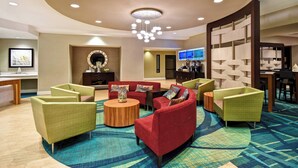 A lobby with a round wooden coffee table, red sofas, green armchairs, and a large TV screen. - SpringHill Suites by Marriott Baltimore BWI Airport (Linthicum Heights)