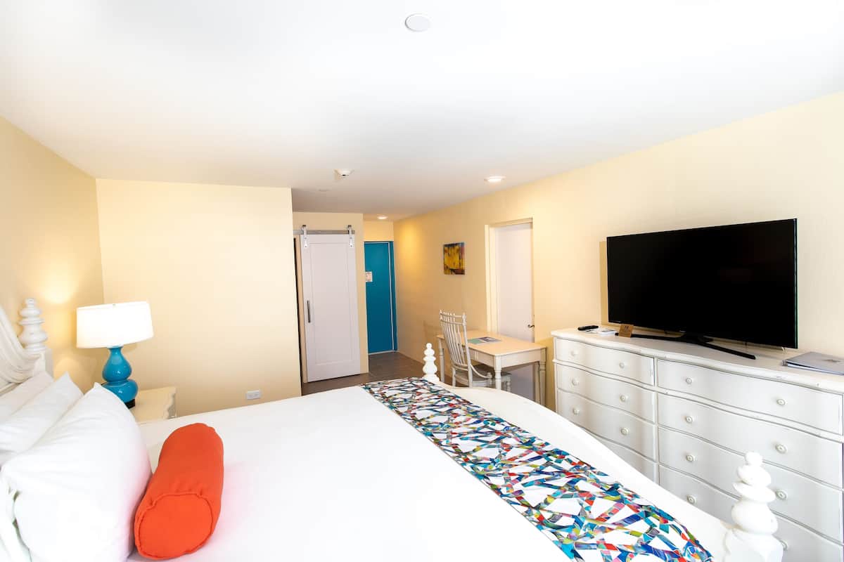 Una habitación de hotel con cama, escritorio, televisión y cómoda.