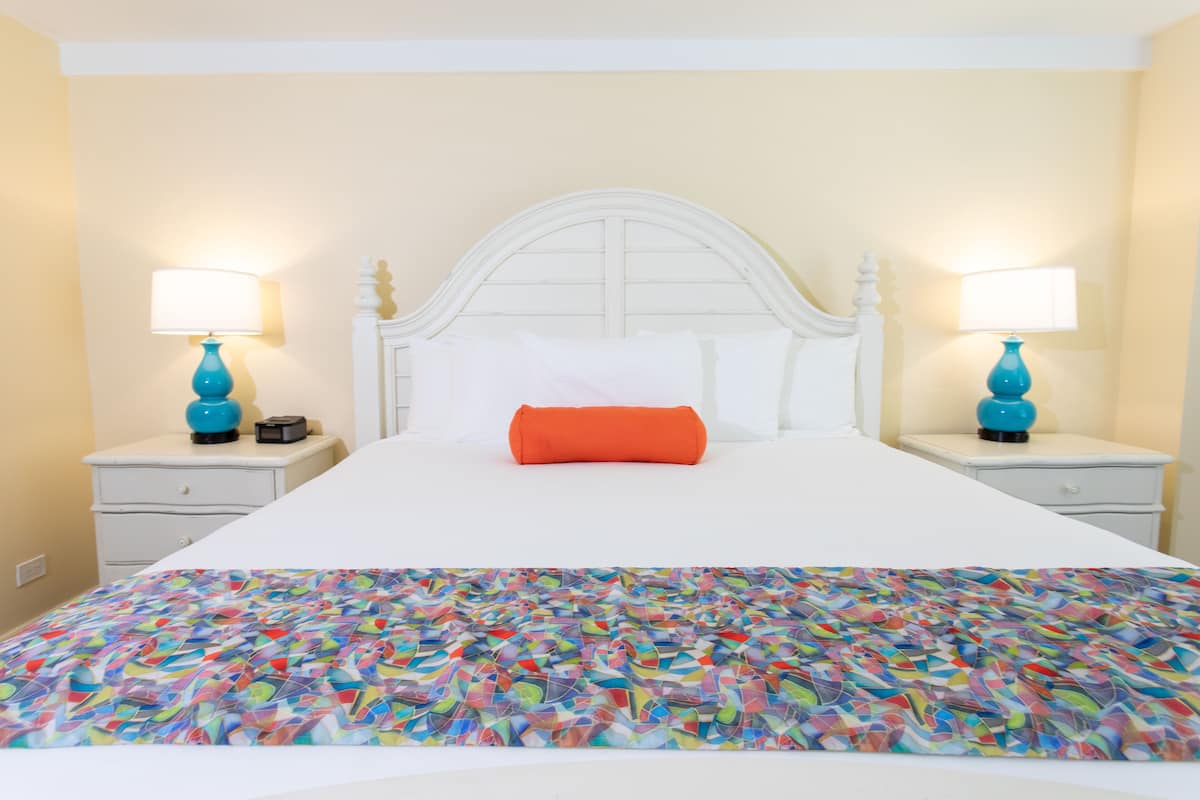 Una cama con un edredón colorido, cabecera blanca y dos mesitas de noche con lámparas.
