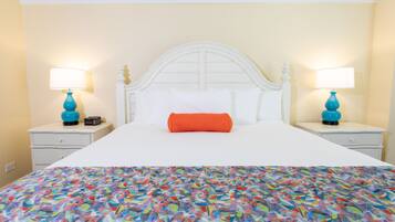 Un llit amb un llençol de colors, un capçal blanc i dues tauletes de nit amb làmpades.