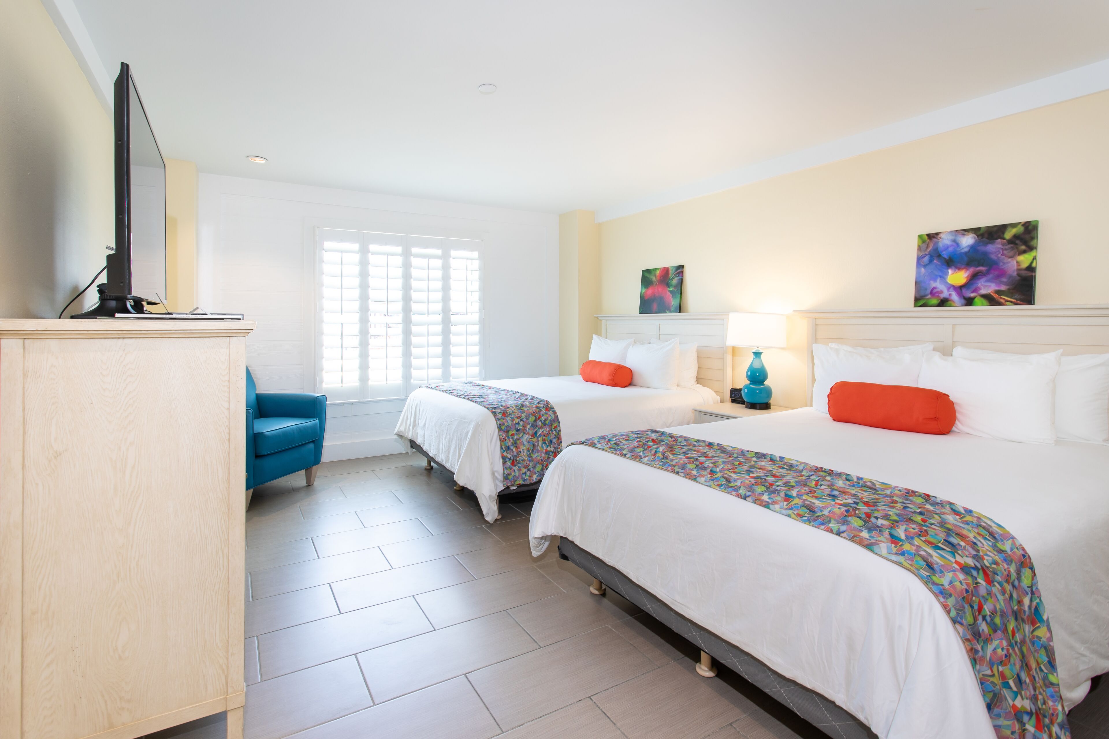Een hotelkamer met twee bedden, een bureau, een stoel en kunstwerken aan de muur.
