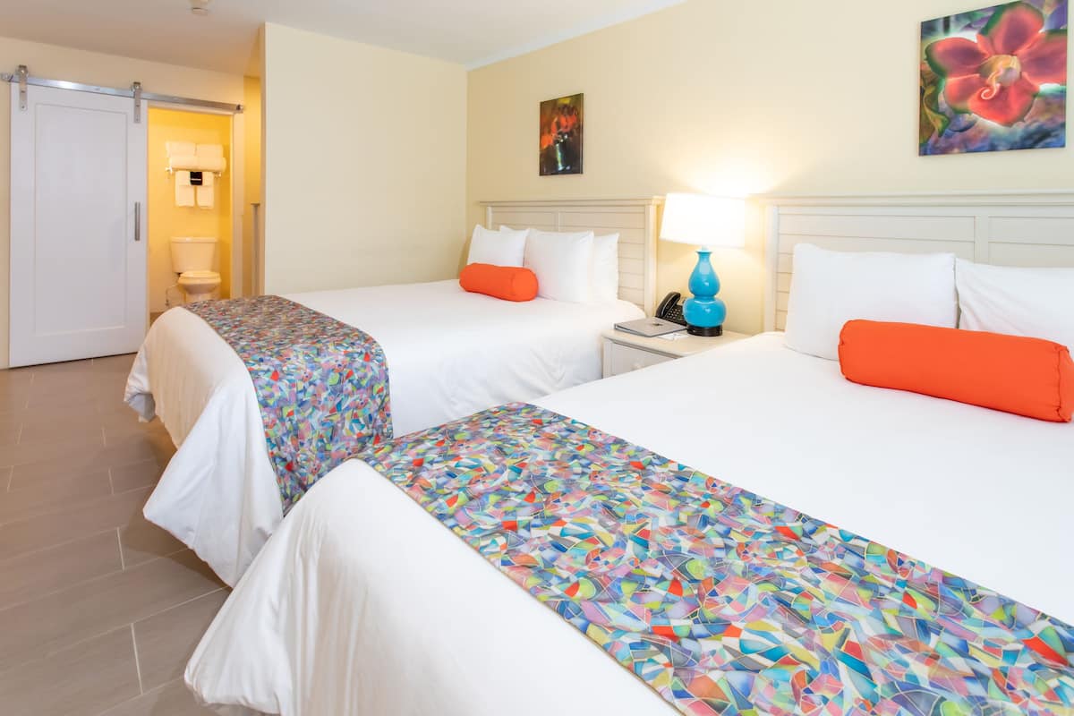 Habitación de hotel con dos camas, un baño y una mesita de noche con lámpara.
