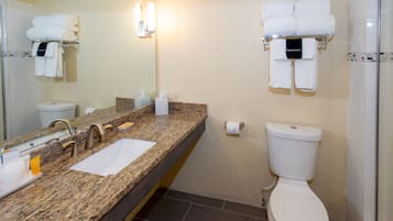 A bathroom with a granite countertop, a sink, a mirror, a toilet, and a towel rack with folded towels.