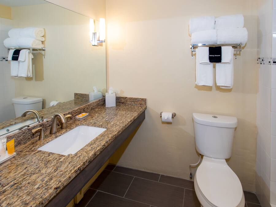 A bathroom with a granite countertop, a sink, a mirror, a toilet, and a towel rack with folded towels.