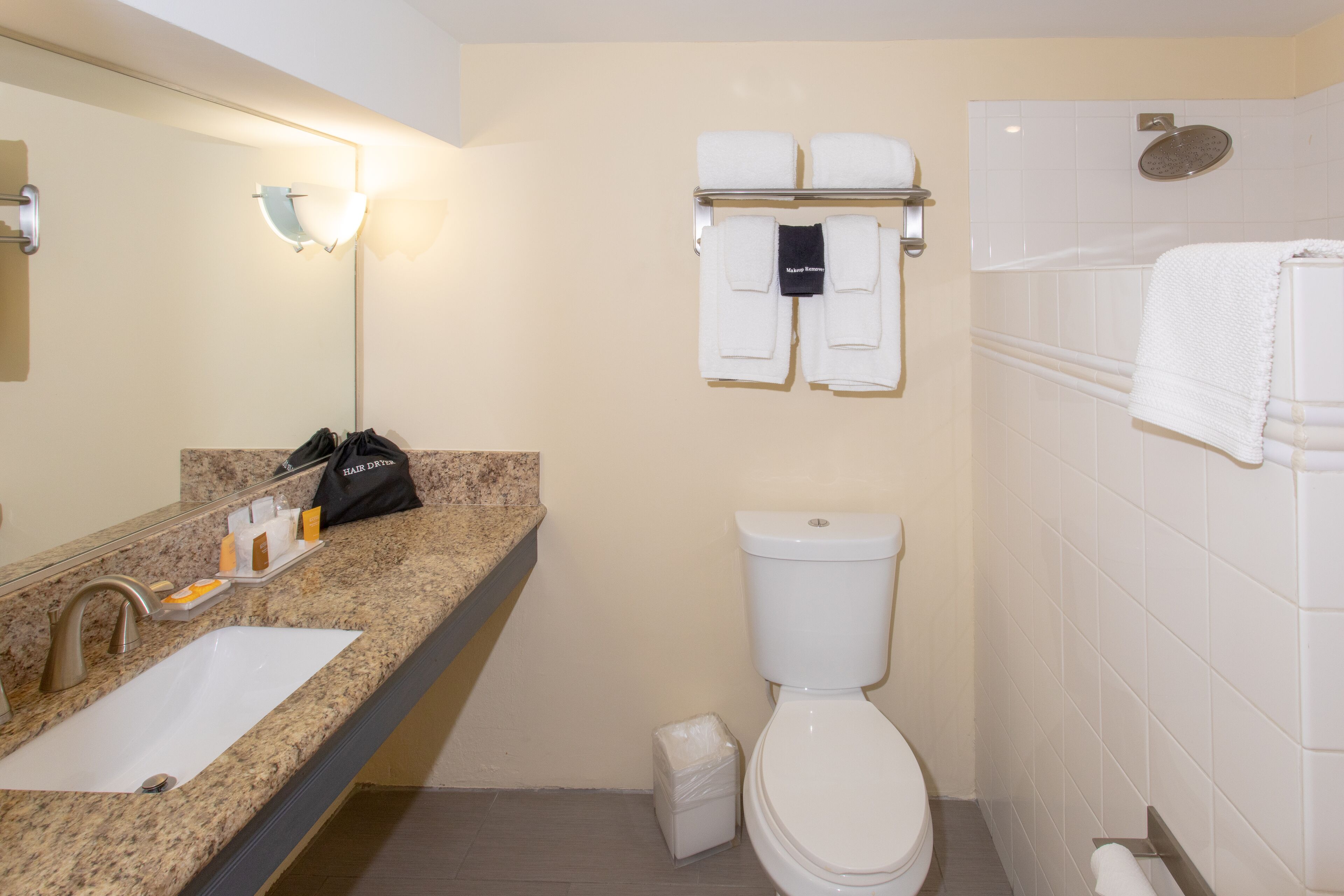 Ein Badezimmer mit Waschbecken, Toilette und Duschbereich. Auf der Ablage liegen Handtücher und Pflegeprodukte.