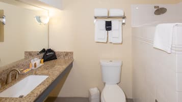 Ein Badezimmer mit Waschbecken, Toilette und Duschbereich. Auf der Ablage liegen Handtücher und Pflegeprodukte.