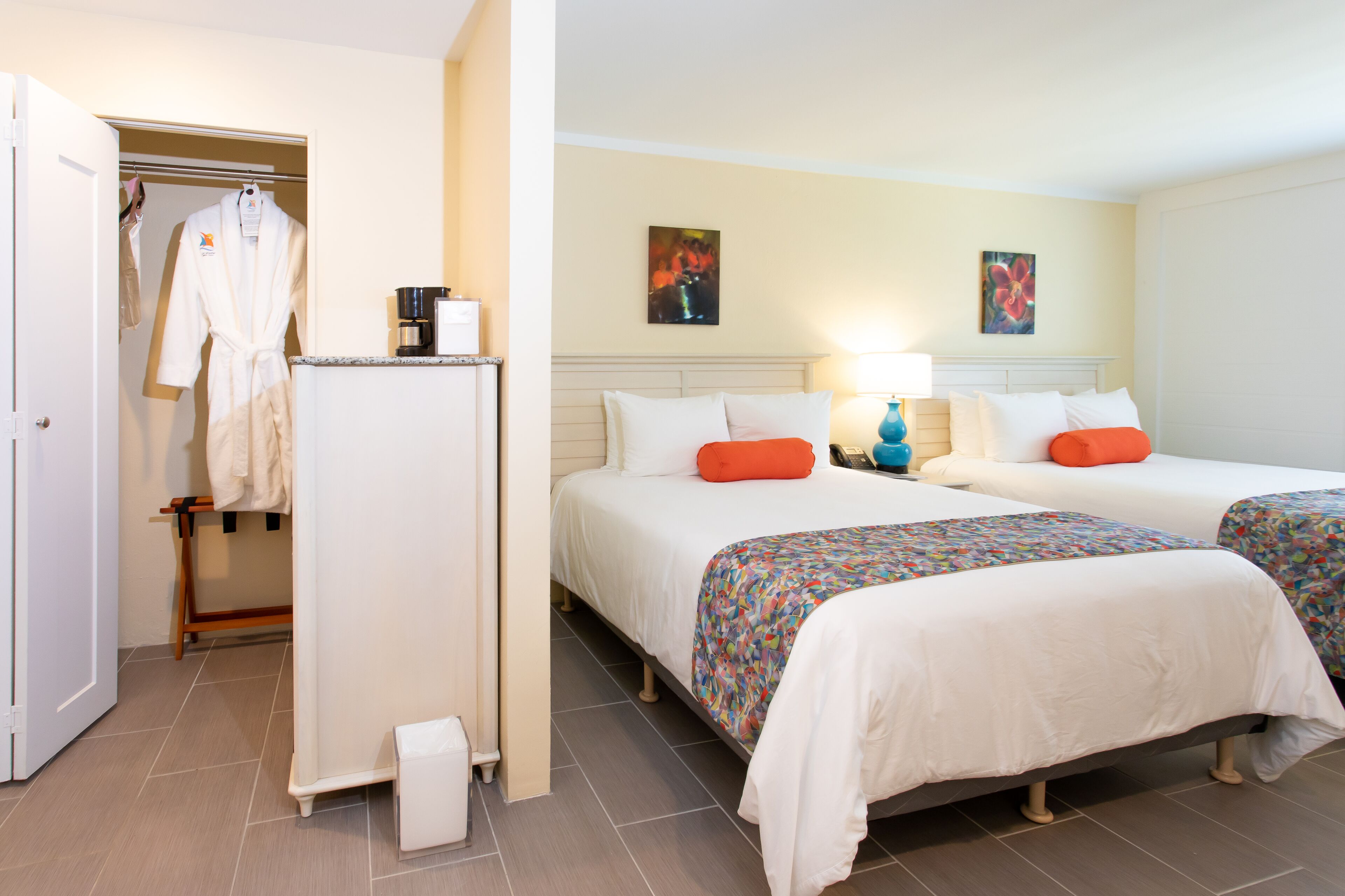 A hotel room with two beds, a wardrobe, a coffee maker, and artwork on the walls.