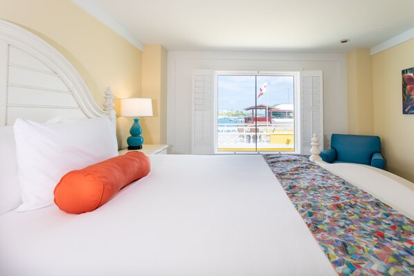 Relax in a spacious room with a large bed, white linens, and a colorful runner. Enjoy a view of the city from the large window.