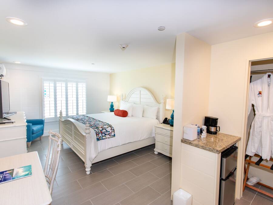 A hotel room with a bed, bedside tables, a desk, a chair, a robe rack, and a bathroom.