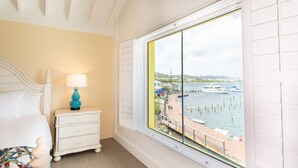 Un dormitorio con cama, una mesita de noche con lámpara y un ventanal con vistas al puerto deportivo.