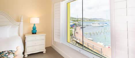 A bedroom with a bed, a nightstand with a lamp, and a large window with a view of a marina.