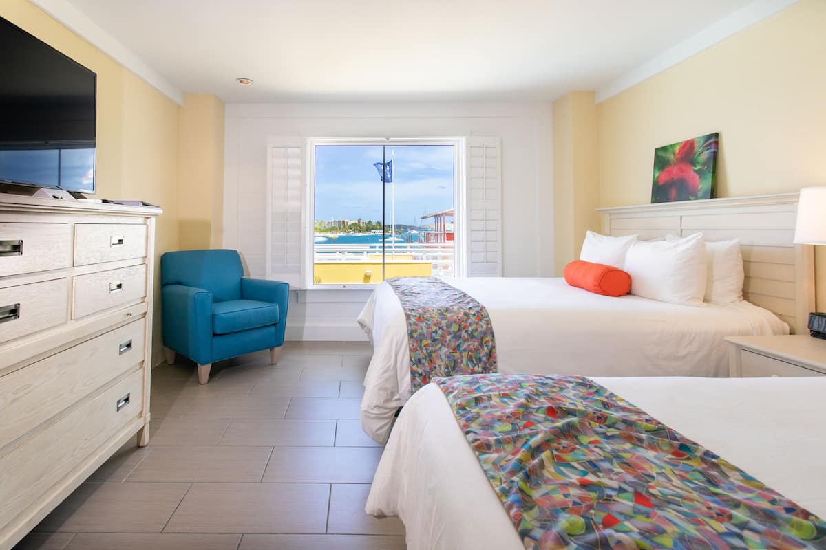 Habitación de hotel con dos camas, televisión, una silla y vista al mar.