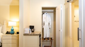 Habitación de hotel con cama, mesita de noche con lámpara, cafetera, bata colgada en un perchero y armario.