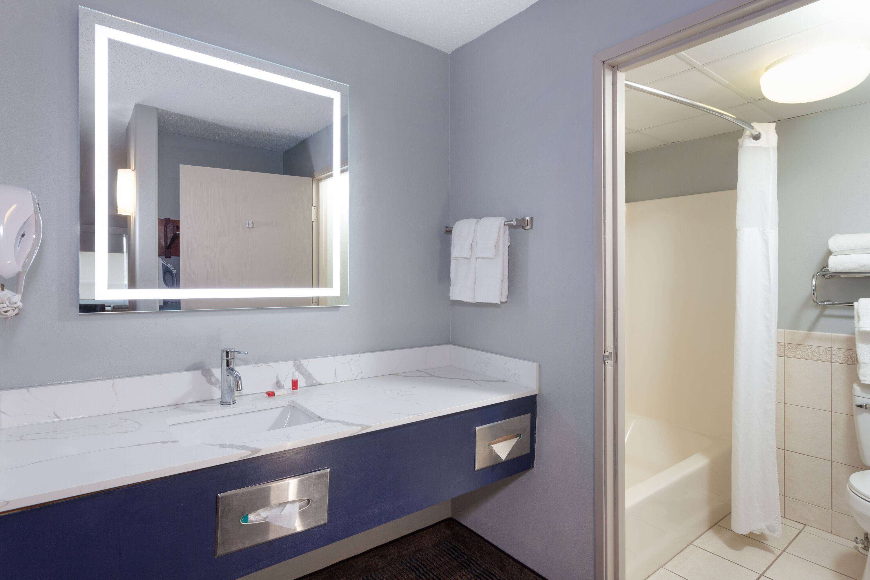A bathroom with a large mirror, a sink with a faucet, a towel rack, and a shower area.