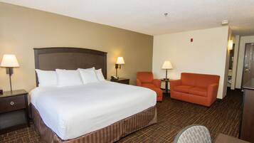 Una habitación de hotel con una cama grande, dos sillas, un escritorio y una lámpara.