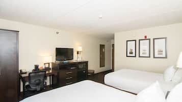 A hotel room with two beds, a desk with a television, a chair, and a small table with a lamp.
