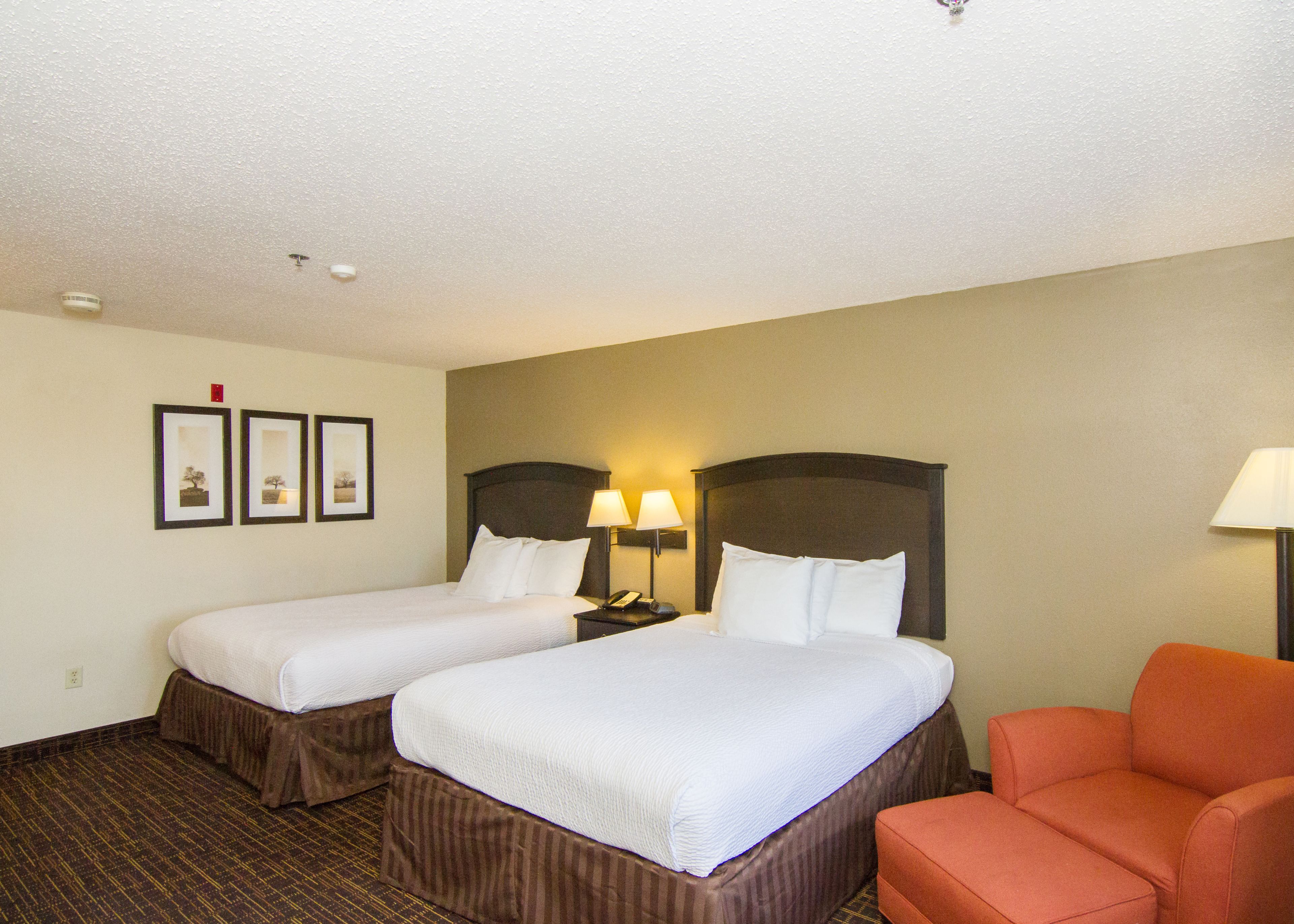 A hotel room with two beds, a nightstand with lamps, a chair, and framed pictures on the wall.