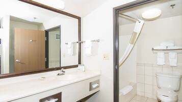 A hotel bathroom with a large mirror, a sink, a toilet, and a shower.