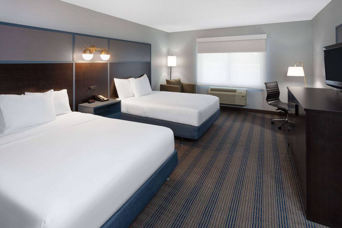 A hotel room with two beds, a desk, a chair, a TV, and a window with blinds.