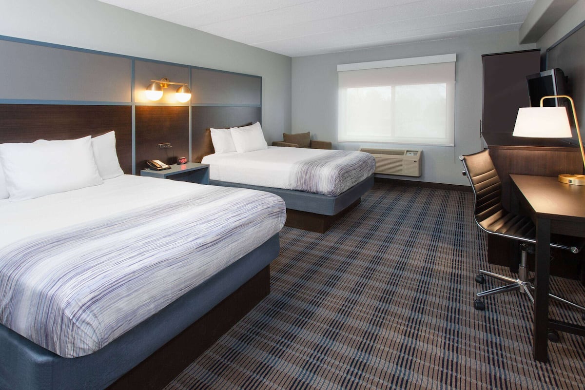 A hotel room with two beds, a desk, a chair, a TV, and a window.