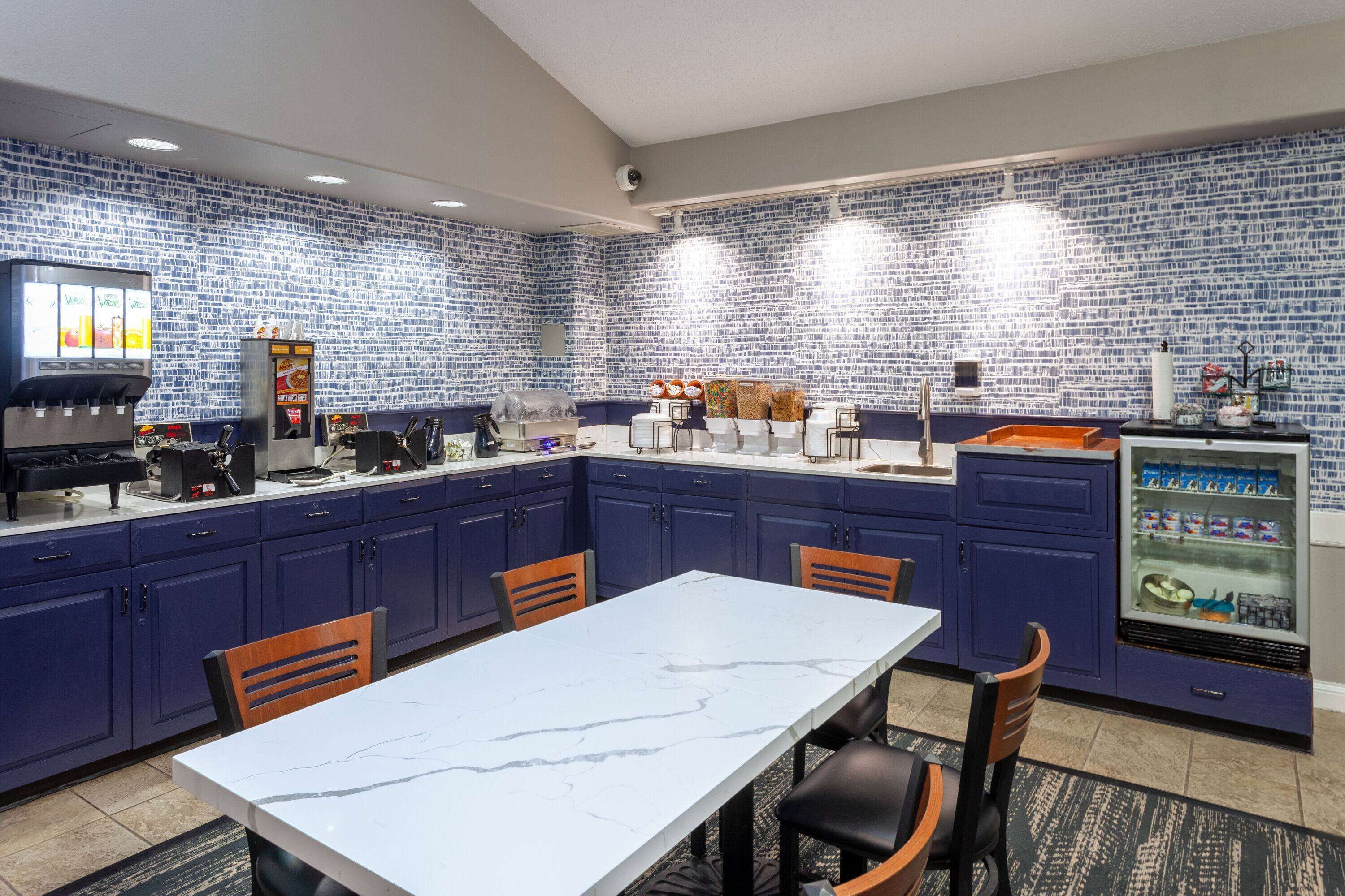 A kitchen with blue cabinets, a marble countertop, and a refrigerator with a beverage dispenser.