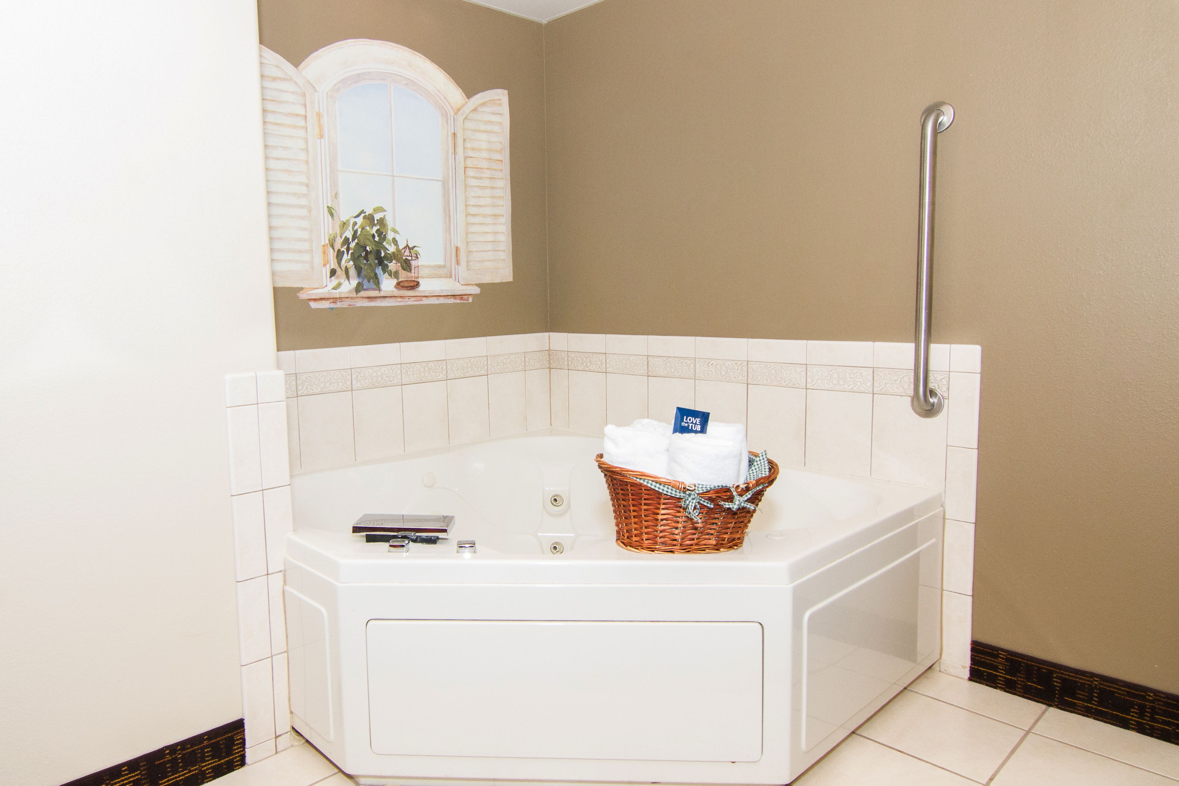 Une salle de bain avec une baignoire, une fenêtre avec des volets, un porte-serviettes et une barre d’appui.