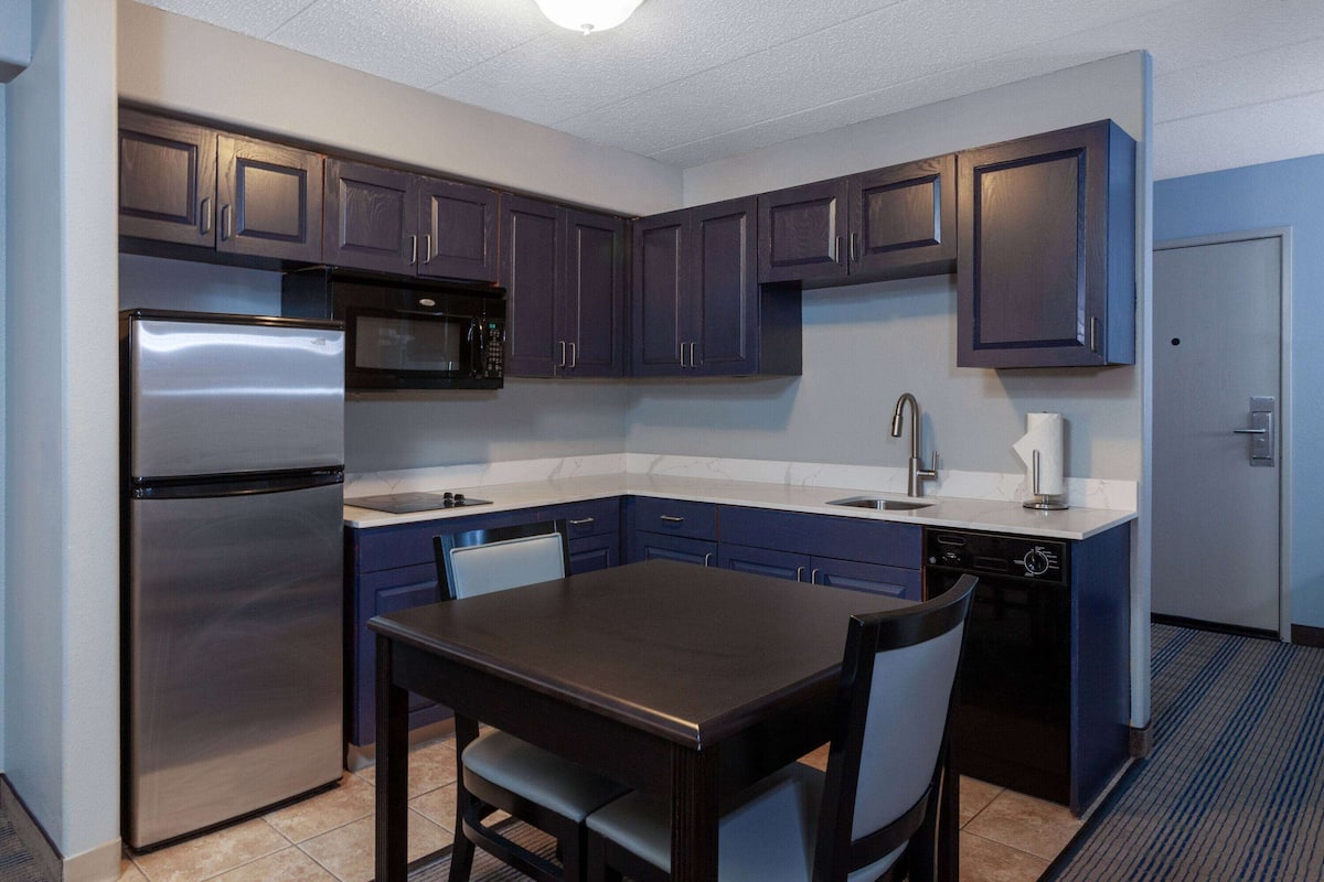 A compact kitchen with dark cabinets, a stainless steel refrigerator, a microwave, a sink, and a dishwasher.