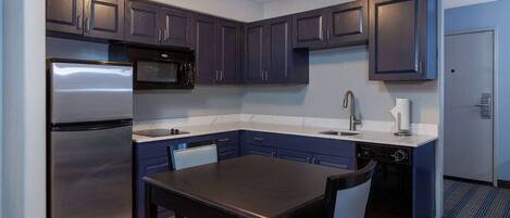A compact kitchen with dark cabinets, a stainless steel refrigerator, a microwave, a sink, and a dishwasher.