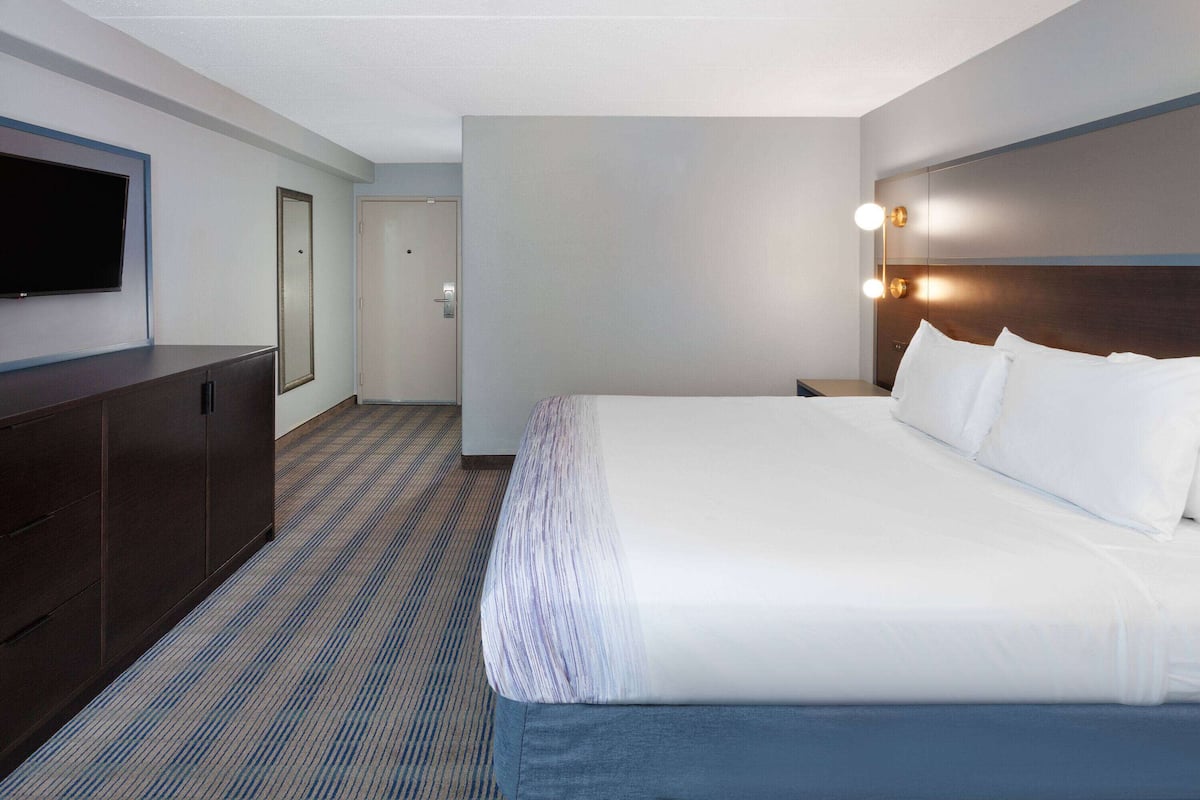 A hotel room with a large bed, a flat-screen TV mounted on the wall, a wooden dresser, and a carpeted floor.