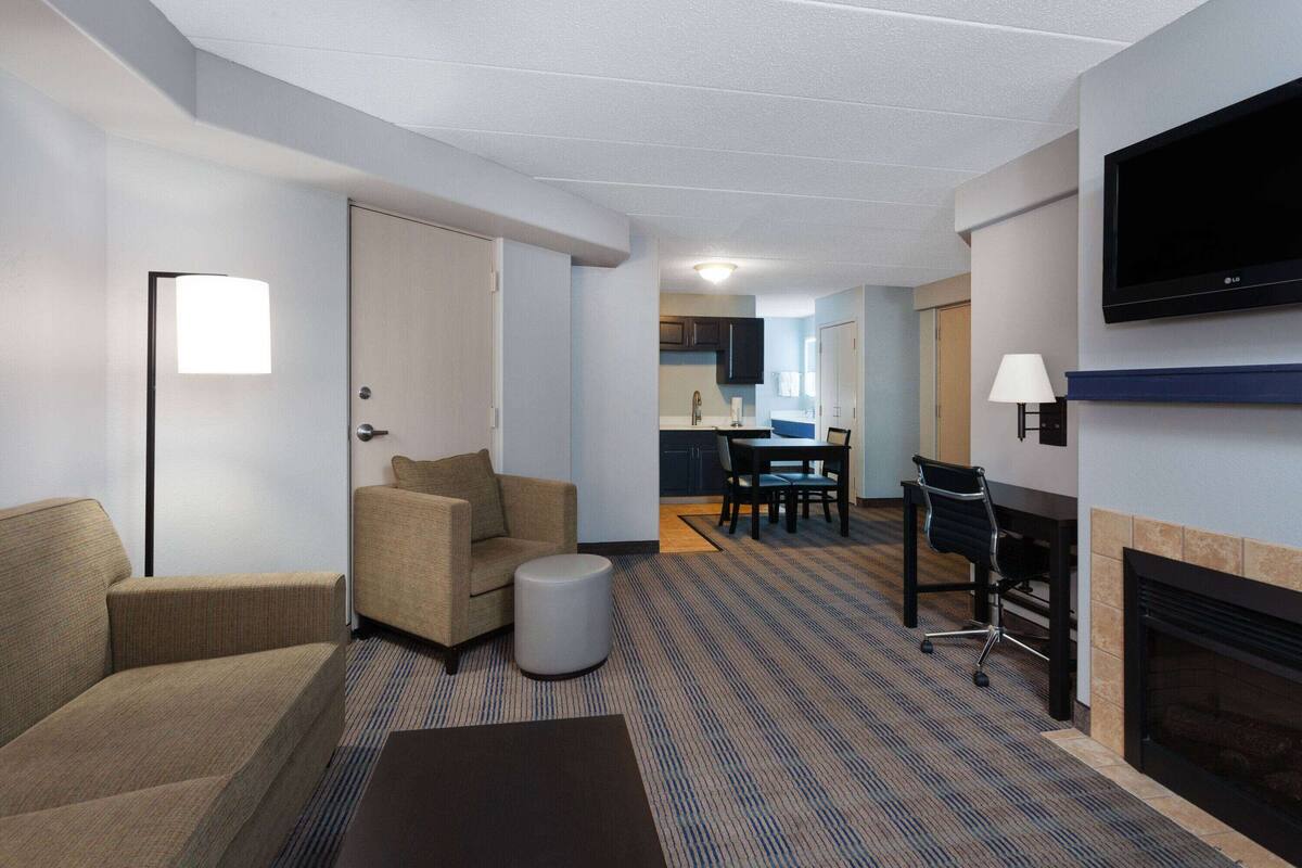 A hotel room with a living area, a dining area, and a TV mounted on the wall.