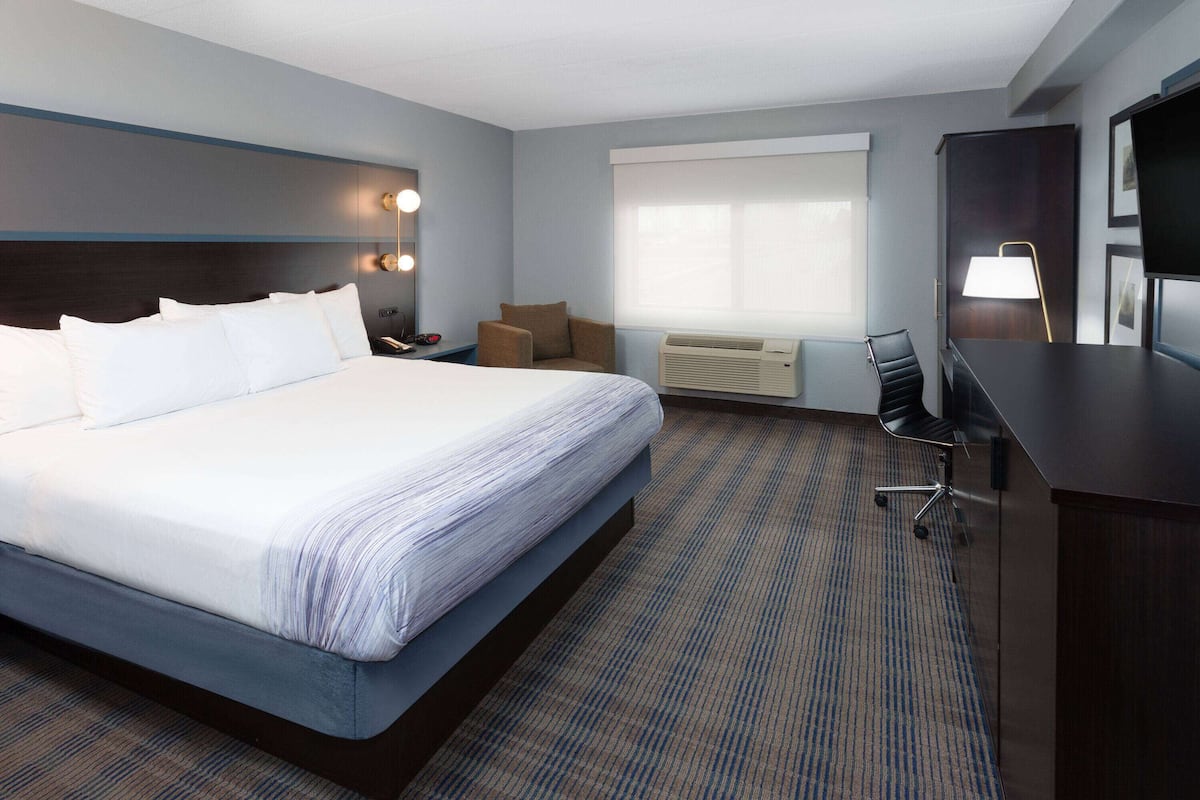 A hotel room with a large bed, a desk with a chair, a TV, and a window with blinds.