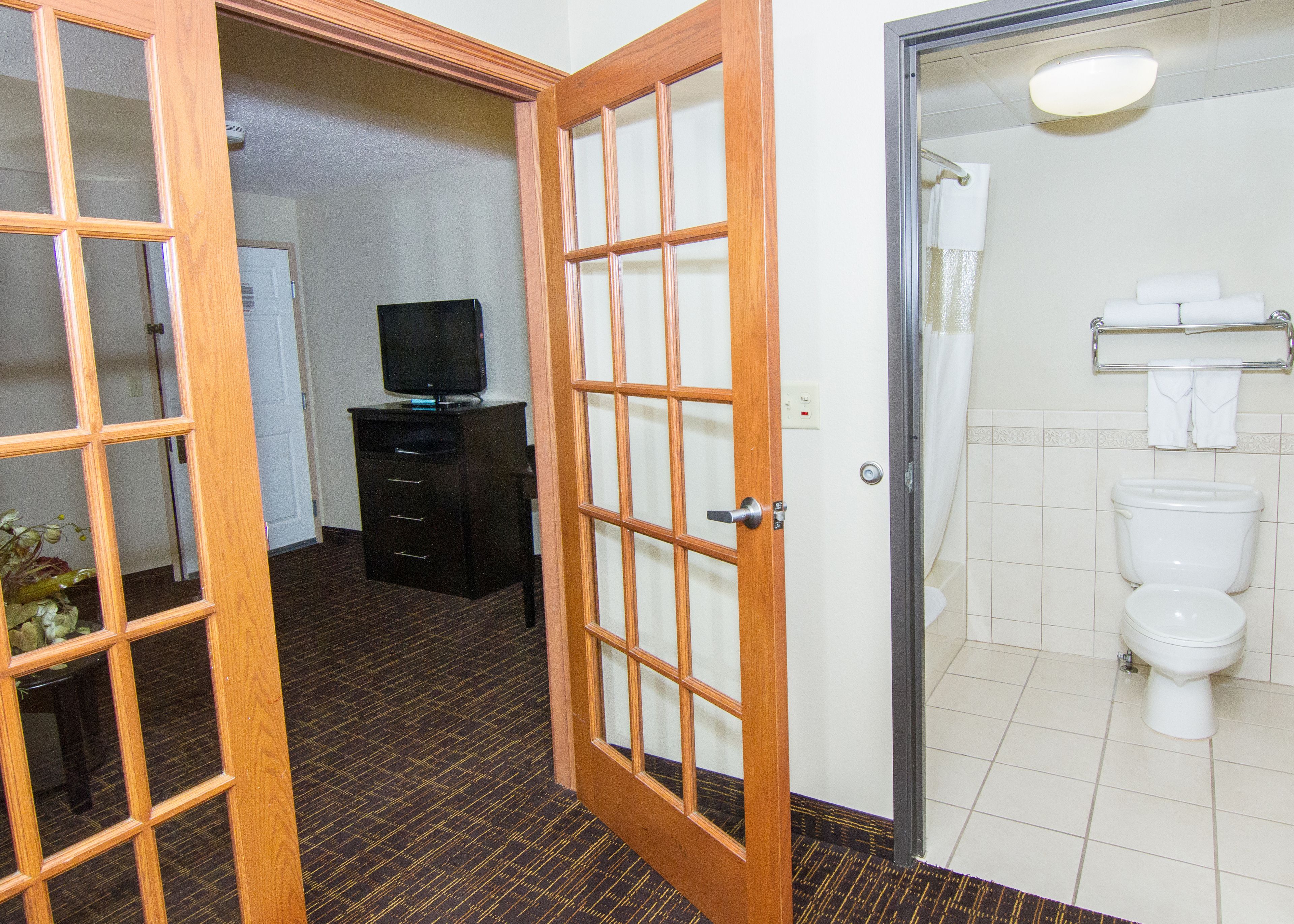 A hotel room with a wooden door, a television on a black cabinet, and a bathroom with a toilet and towel rack.