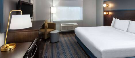 Una habitación de hotel con cama, escritorio, silla, lámpara, televisor y aire acondicionado.