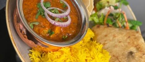 A plate with yellow rice, a bowl of curry garnished with onions and cilantro, a piece of flatbread, and a small salad.