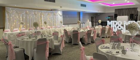 A banquet hall with round tables, each adorned with pink sashes and white tablecloths.