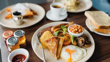 A breakfast setting with plates of food, a cup of coffee, condiments, and a bread roll.